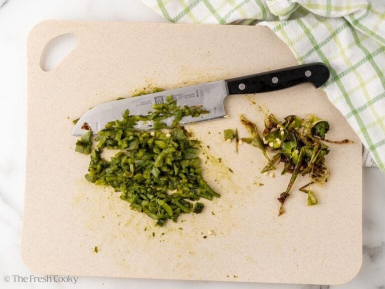 Diced roasted poblano pepper on a wooden board with a chef's knife.