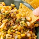 Close up of a tortilla chip being dipped into corn salsa.