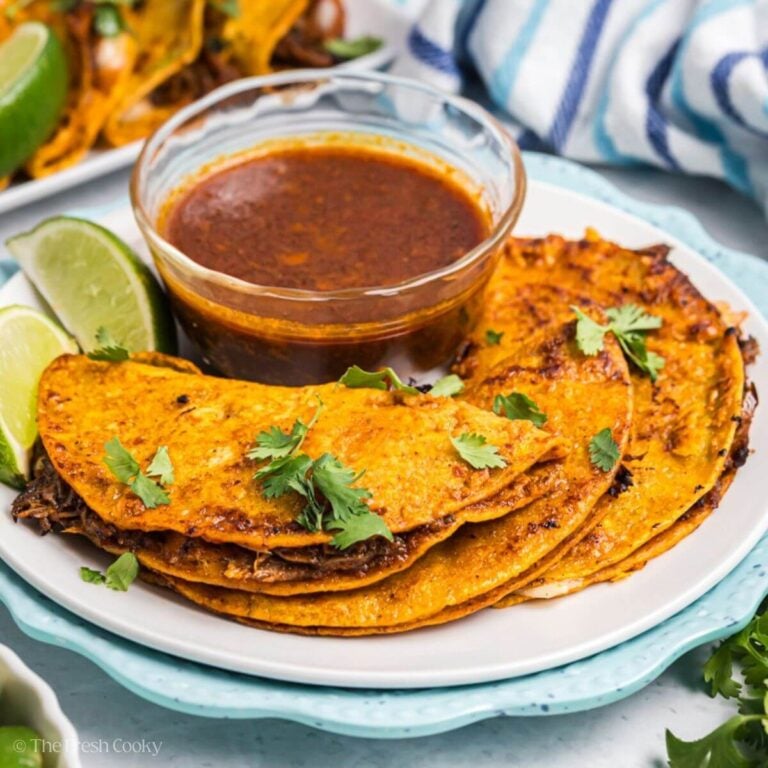 A plate filled with several crispy birria tacos with a. bowl of consommé for dipping.
