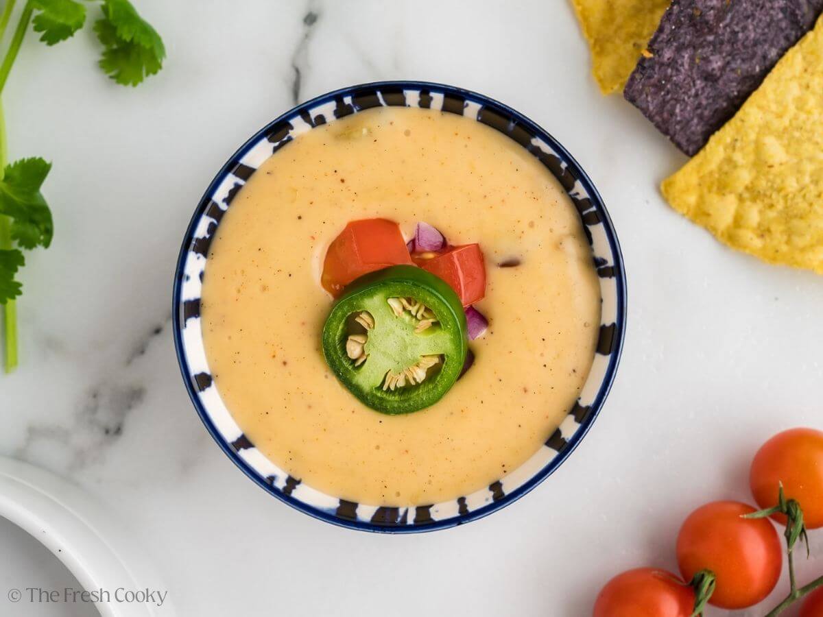 Queso cheese dip in pretty bowl garnished with jalapeno, tomato, cilantro and diced onions.