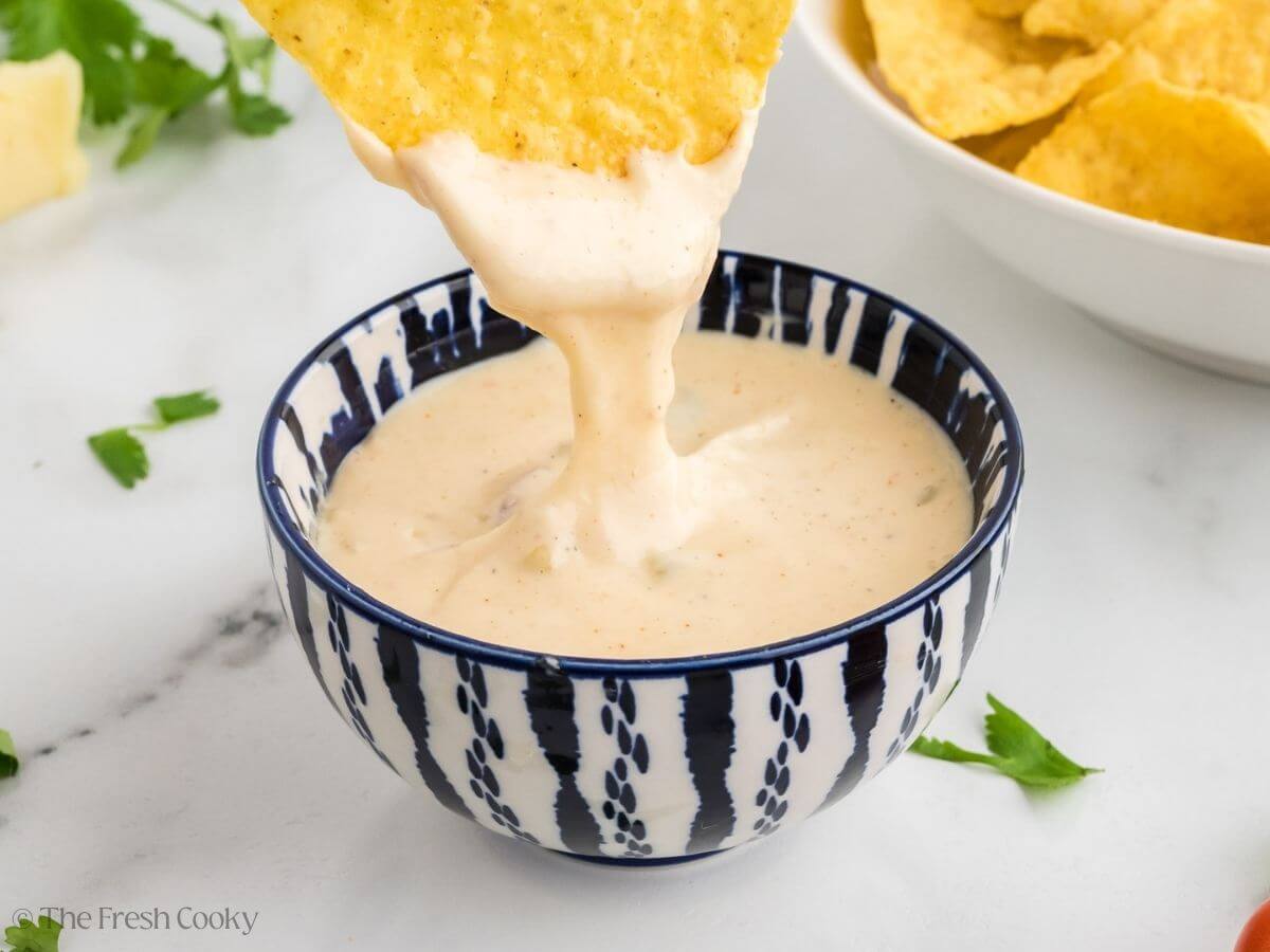 White Queso Dip with a tortilla chip pulling out a cheesy bite.