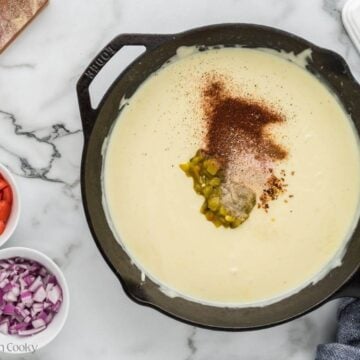 Spices and chiles added into white cheese sauce in pan.