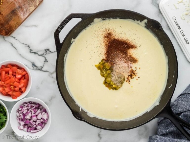 Spices and chiles added into white cheese sauce in pan.