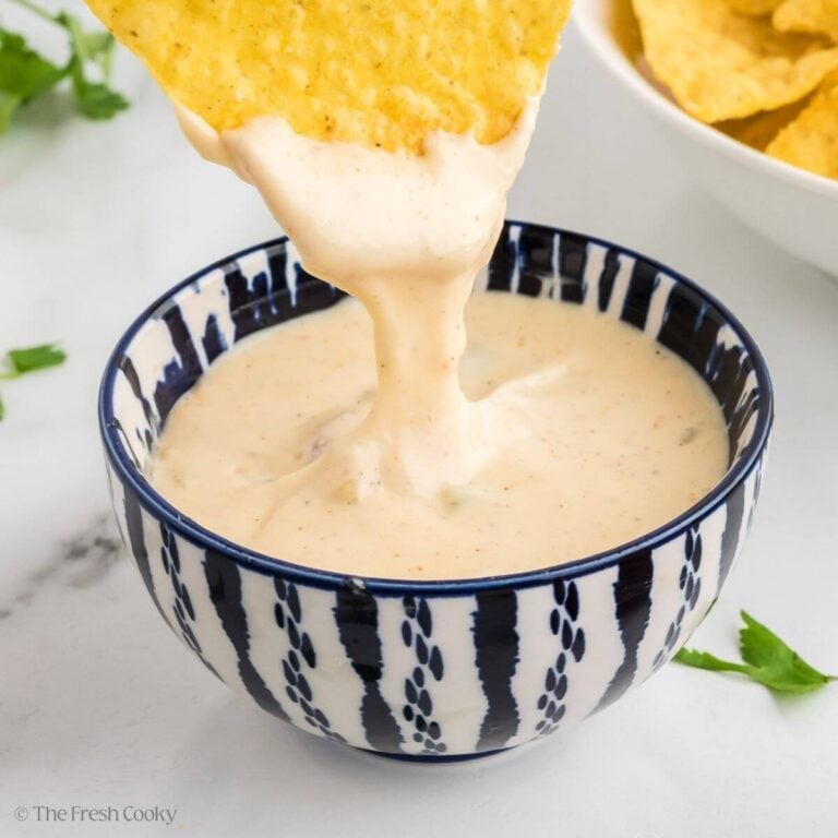 Tortilla chip being dipped into cheesy queso dip.
