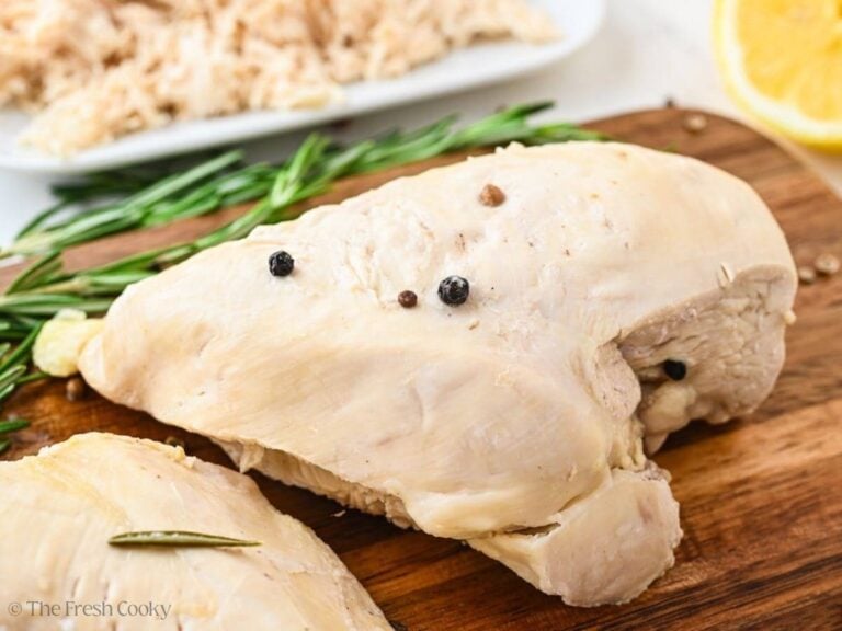 Poached chicken breast on a wooden cutting board with peppercorns on it.