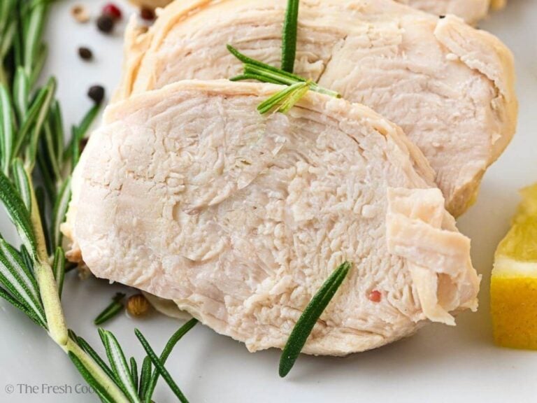 Close up of a slice of poached chicken next to a sprig of rosemary.
