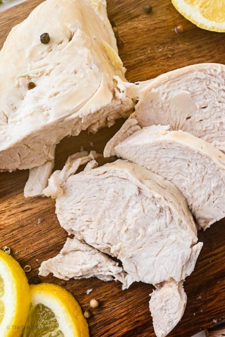 Overhead shot of three slices of poached chicken on a wooden cutting board.