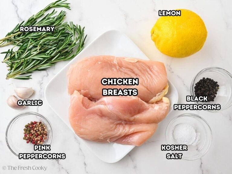 Labeled ingredients for how to poach chicken: L-R Fresh herbs (rosemary, chicken breasts, lemon, black peppercorns, kosher salt, pink peppercorns, garlic.