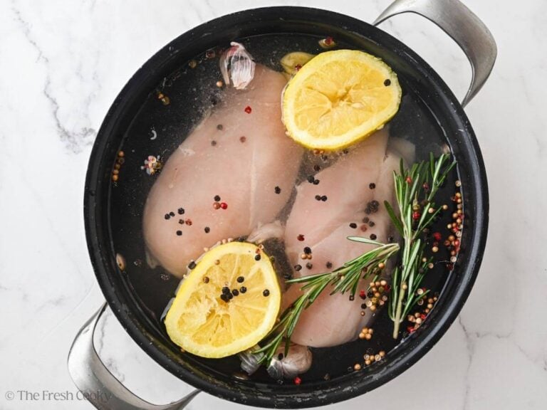 Lemon, herbs, garlic, and peppercorns added to the chicken breasts and water in a pot.
