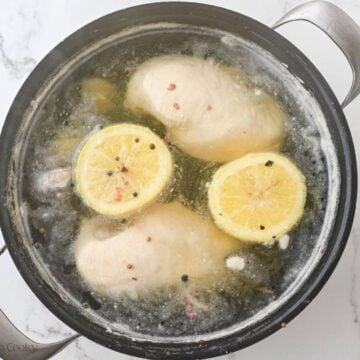 Chicken breasts in a pot of boiling water with aromatics.