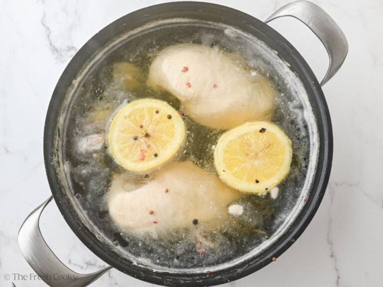 Chicken breasts in a pot of boiling water with aromatics.