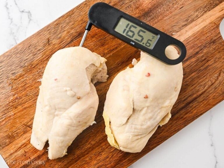 Two pieces of poached chicken on a wooden cutting board with a thermometer sticking out of one of them registering at 165.