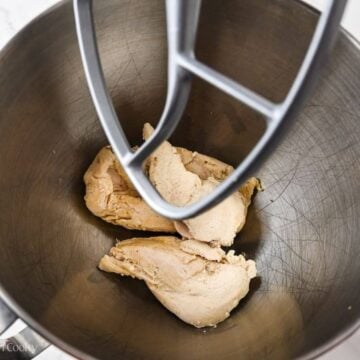Poached chicken breasts in the bowl of a stand mixer with a paddle attachment.