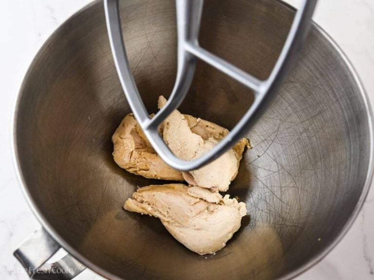 Poached chicken breasts in the bowl of a stand mixer with a paddle attachment.