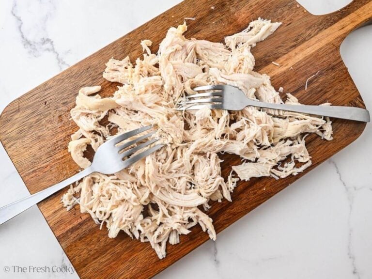 Shredded chicken with two forks on a wooden cutting board.