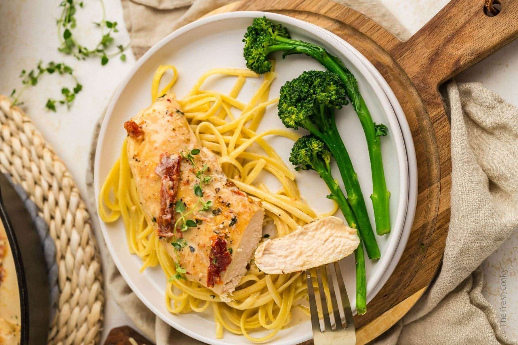 Plate with pasta, marry me chicken, and broccoli with a fork taking a piece of the chicken off.