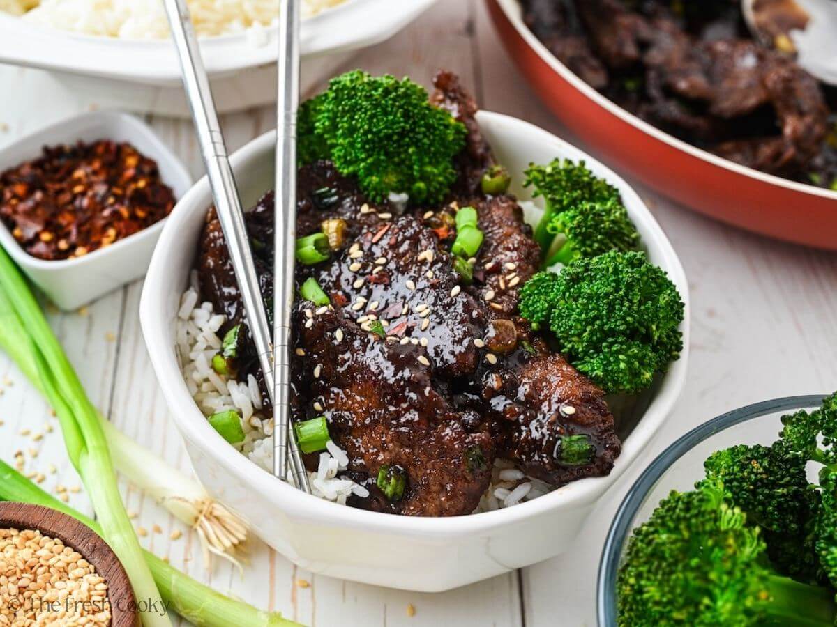 Mongolian beef over rice with broccoli in a bowl with chopsticks.