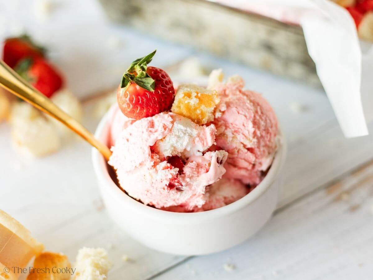 A bowl filled with strawberry shortcake ice cream topped with a fresh strawberry.