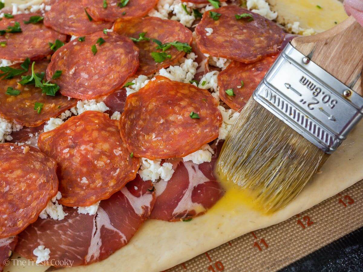 Brushing egg wash on the edges of the pizza dough.