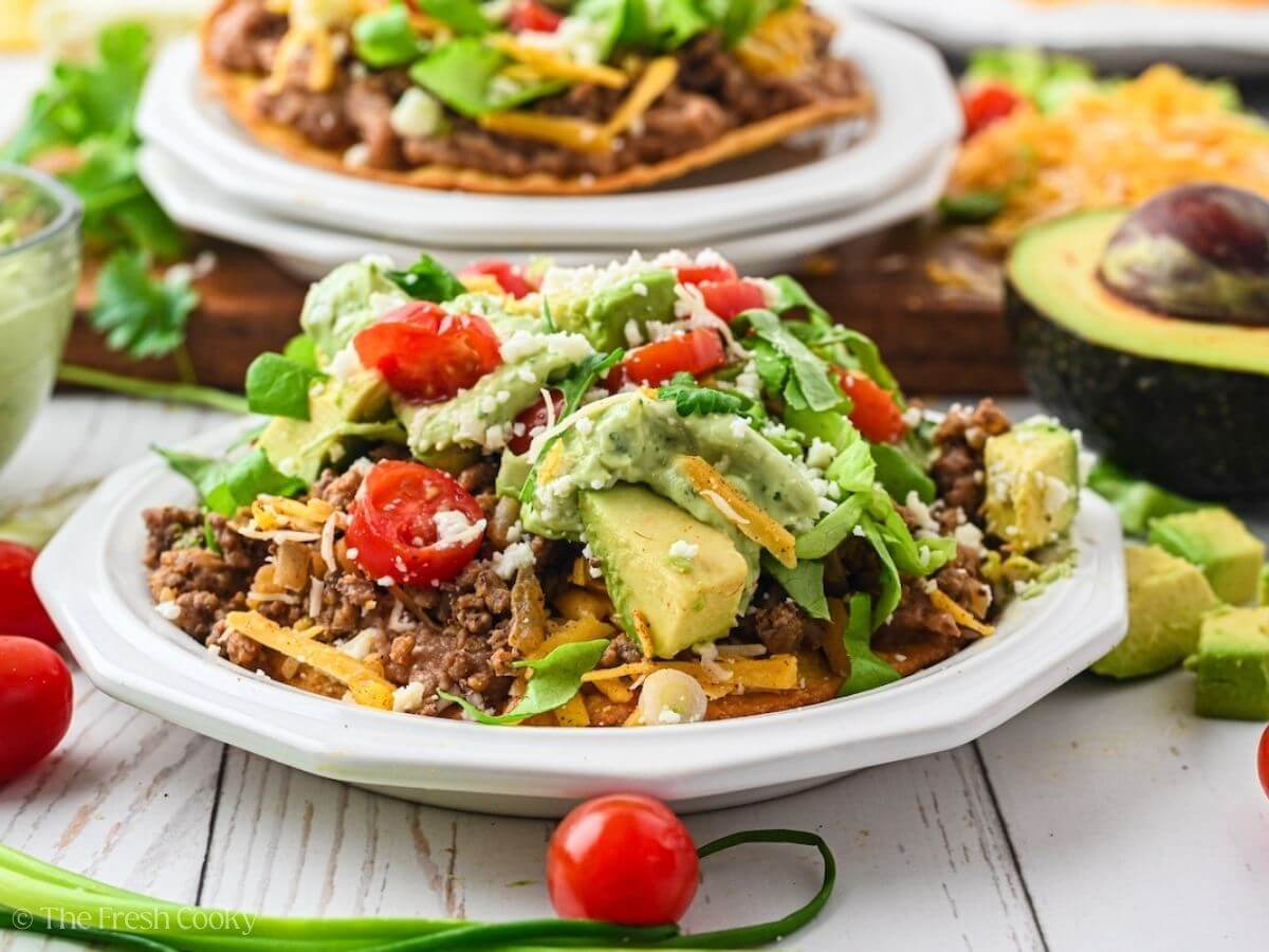 A couple of tostadas on plates, loaded high with beans, meat and toppings.