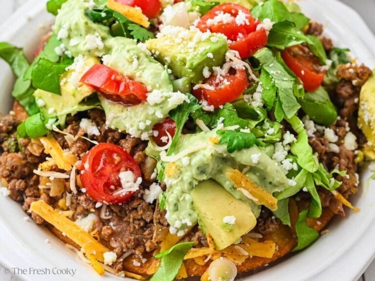 Close up of a tostada, loaded with beans, cheese, meat and toppings.