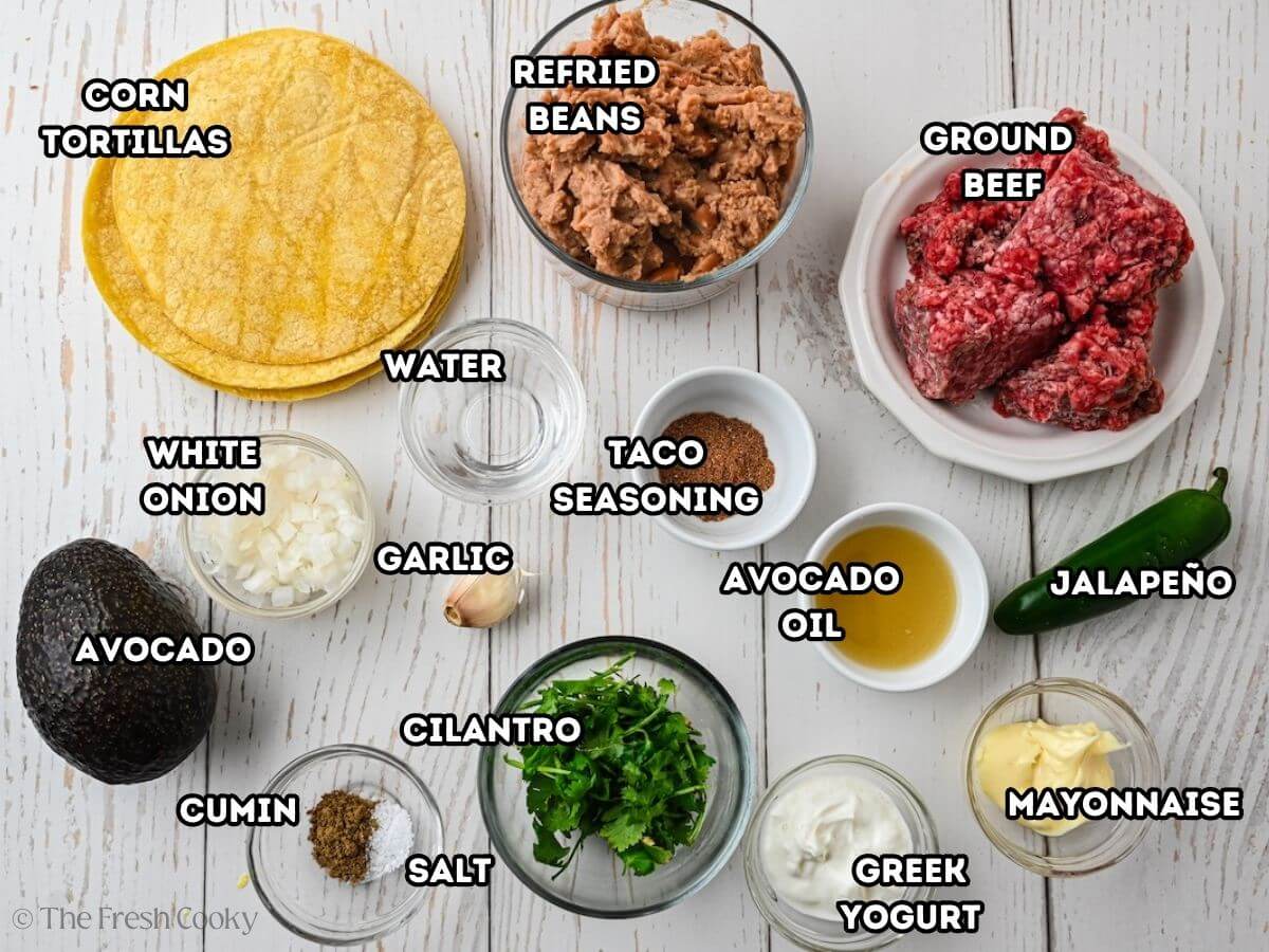 Tostada ingredients, L-R corn tortillas, refried beans, ground beef, jalapeno, mayo, Greek yogurt, avocado oil, taco seasoning, cilantrol, salt, cumin, garlic, water, white onion and avocado.