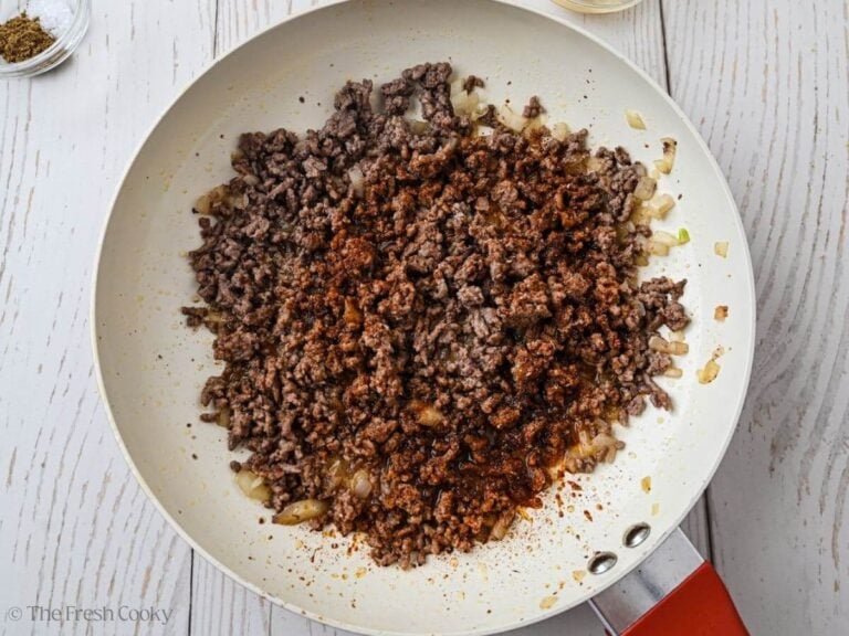 Browned ground beef with seasonings in skillet.