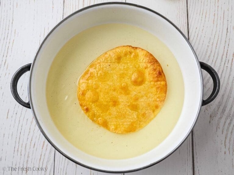 Frying a corn tortilla until crispy in oil in a skillet.