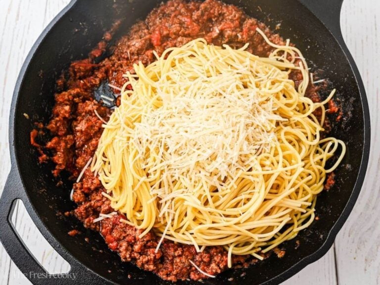 Cooked spaghetti being stirred into meat sauce with cheese.
