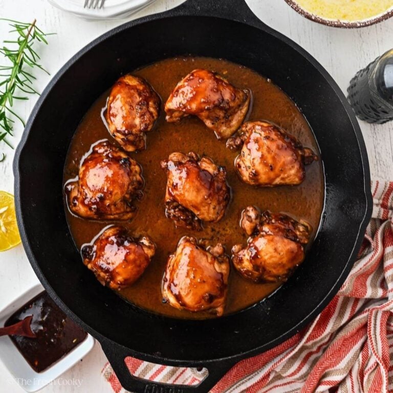 Balsamic chicken thighs in cast iron pan surrounded by polenta, rosemary and lemon.