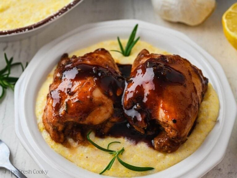 Two balsamic chicken thighs on a bed of polenta on a plate.