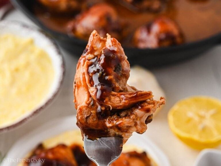 Piece of balsamic chicken on a fork hovering over a plate of chicken.