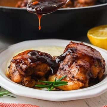 Spooning balsamic glaze over chicken thighs on a plate.