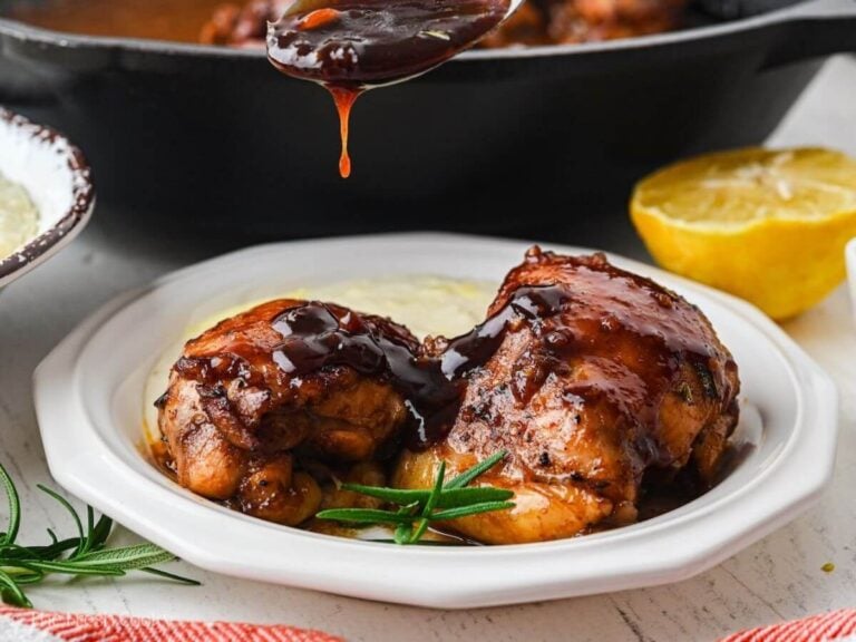 Spooning balsamic glaze over chicken thighs on a plate.
