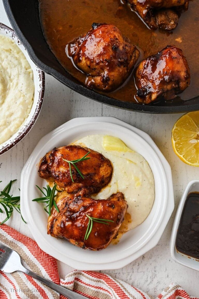 Overhead shot of a plate of polenta and chicken thighs next to a cast iron skillet of balsamic honey chicken.