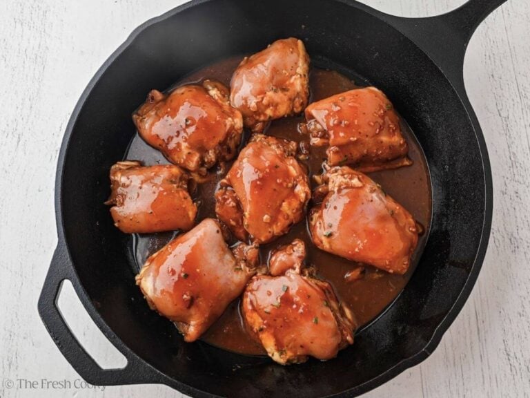 Marinated chicken thighs in a cast iron skillet to cook.