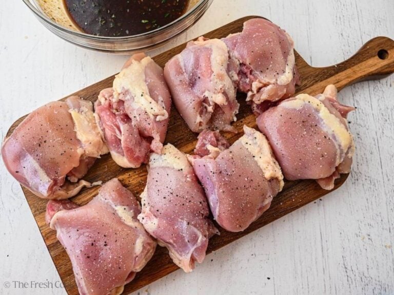 Chicken thighs on a wooden board, seasoned with salt and pepper.