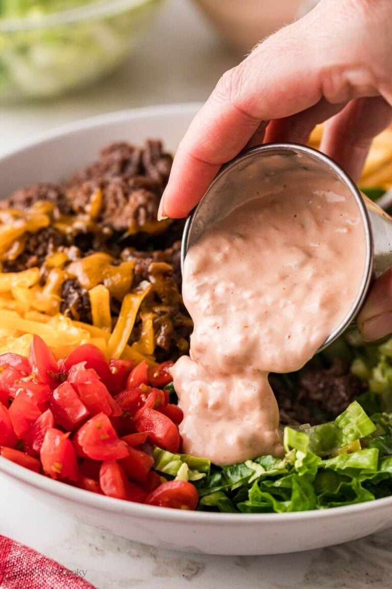 Hand pouring the special sauce over the burger bowl.