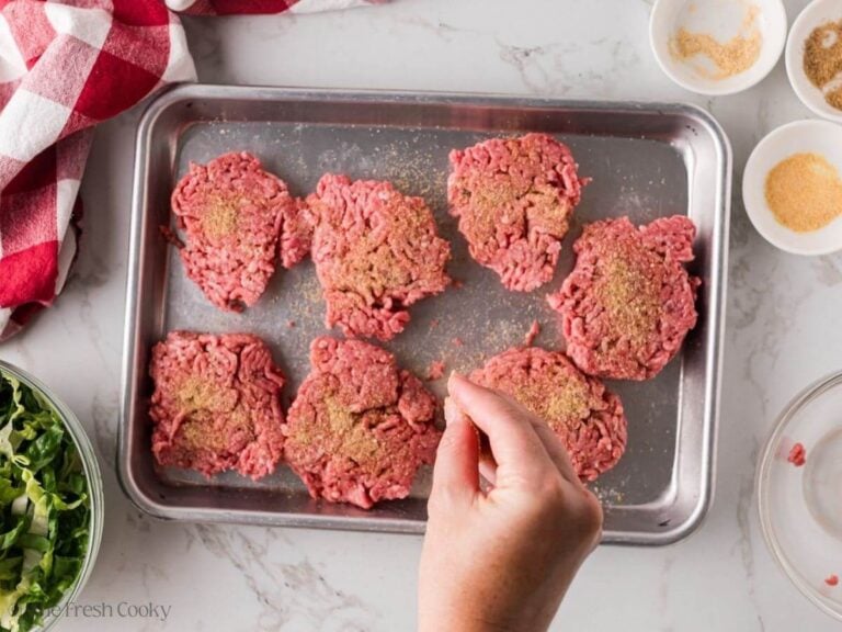 Seasoning hamburger patties on a sheet pan.