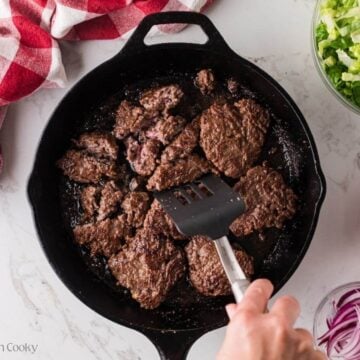 Breaking up the hamburger patties into smaller pieces in a skillet.