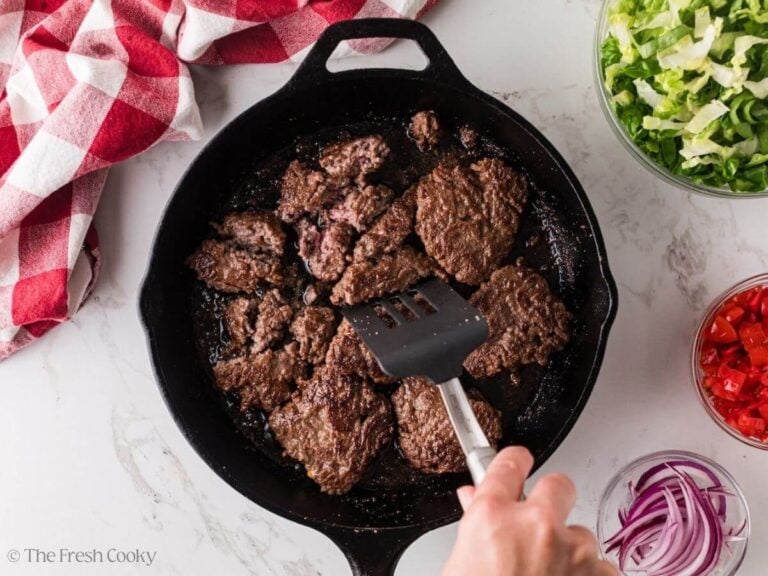 Breaking up the hamburger patties into smaller pieces in a skillet.