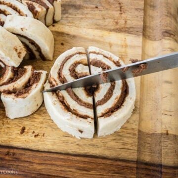 Knife cutting a canned cinnamon roll in quarters.