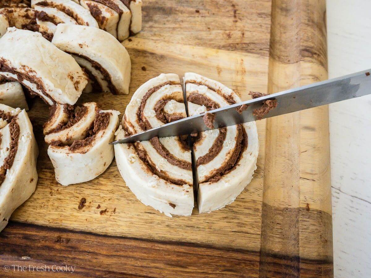 Knife cutting a canned cinnamon roll in quarters.