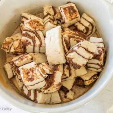 A mixing bowl filled with custard and chopped up canned cinnamon rolls.