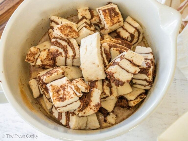 A mixing bowl filled with custard and chopped up canned cinnamon rolls.