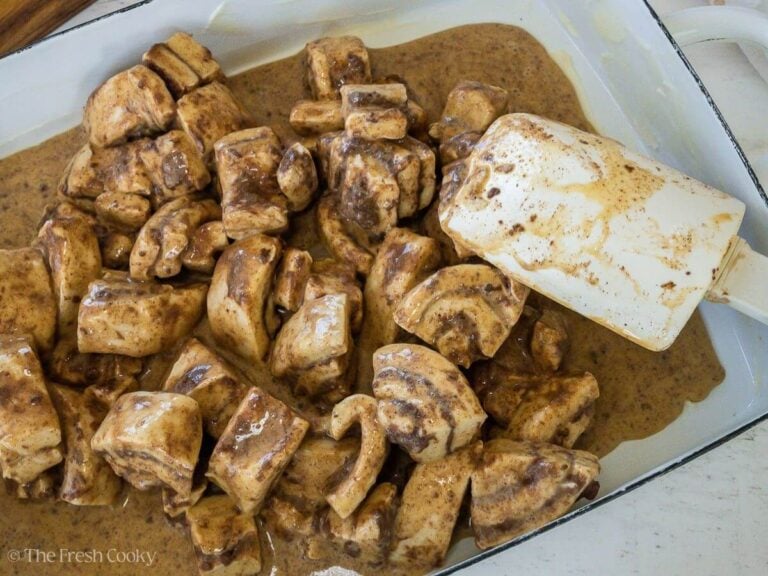 Cinnamon rolls being spread into the baking pan, with custard.