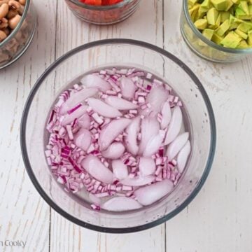 Diced red onion in a bowl with water and ice.