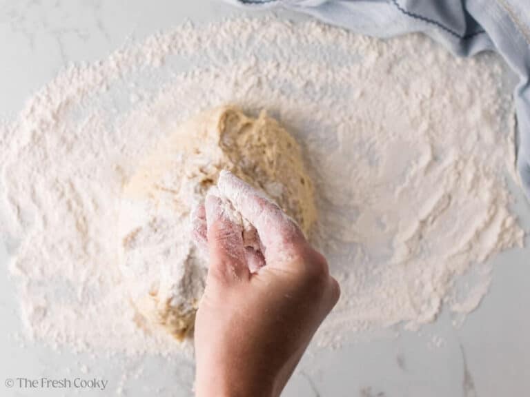 Donut Batter turned out onto a floured surface with a hand sprinkling flour on top.