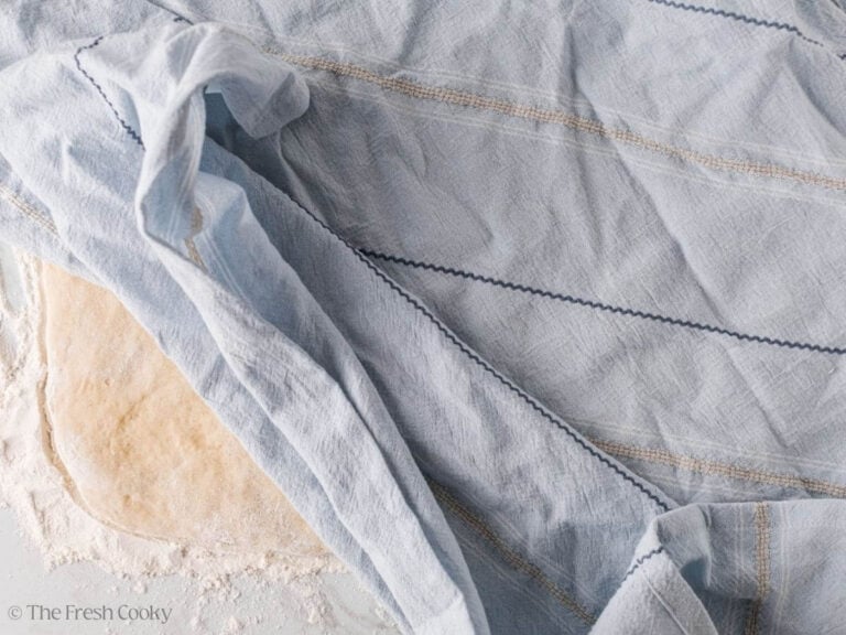 Covering the flattened donut dough with a clean linen.