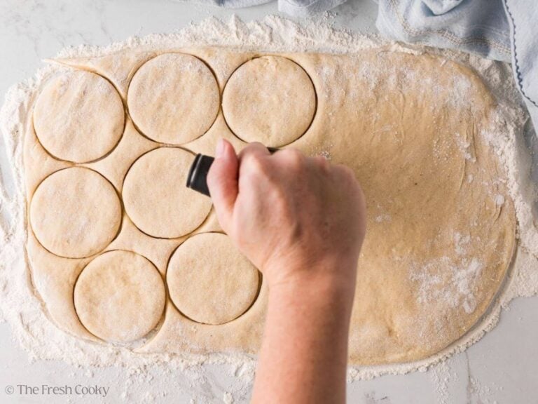 Hand pressing down circles into the donut dough.